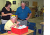 Justine McDonald, left, program operations administrator, explains to APD Director Jim DeBeaugrine how Donald B., sitting, assembles a ClosetMaid bracket.