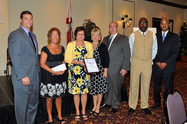 From left, Brian Brown of Avmed Health Plans presents a Notable Cash Award to Gulf Coast Center Closure Team members Sue Rayford, Cindy Millican, Jolie LaTourelle-Jones, Ray Newman, and Michael Mayfield. At right is co-presenter Rep. Chuck Chestnut